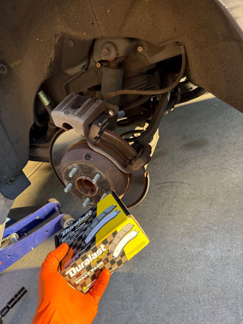 Exposed brake rotor and caliper with a box of brake pads held nearby