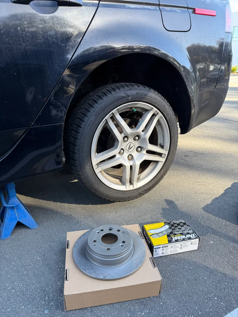 New rotor and brake pads ready next to the car before a mobile brake job