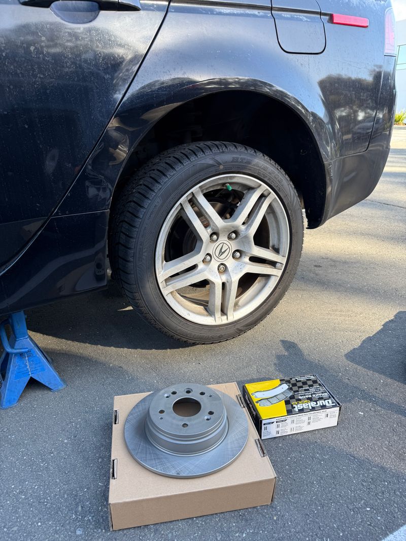Brake rotor and boxed brake pads beside a raised vehicle