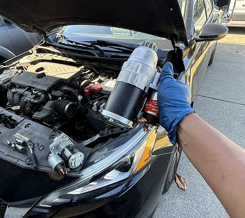 New starter held over a Nissan engine bay during a mobile starter replacement