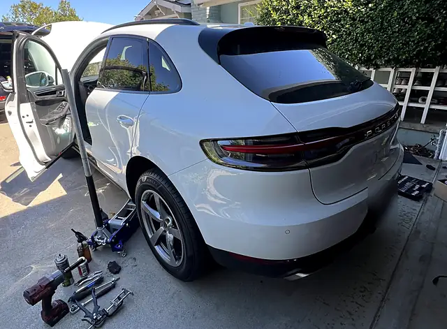 White Porsche Macan on a floor jack with a rear wheel off during a mobile brake service in a customer driveway