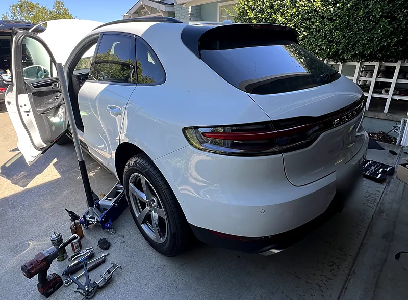 White Porsche Macan on a floor jack with a rear wheel off during a mobile brake service in a customer driveway