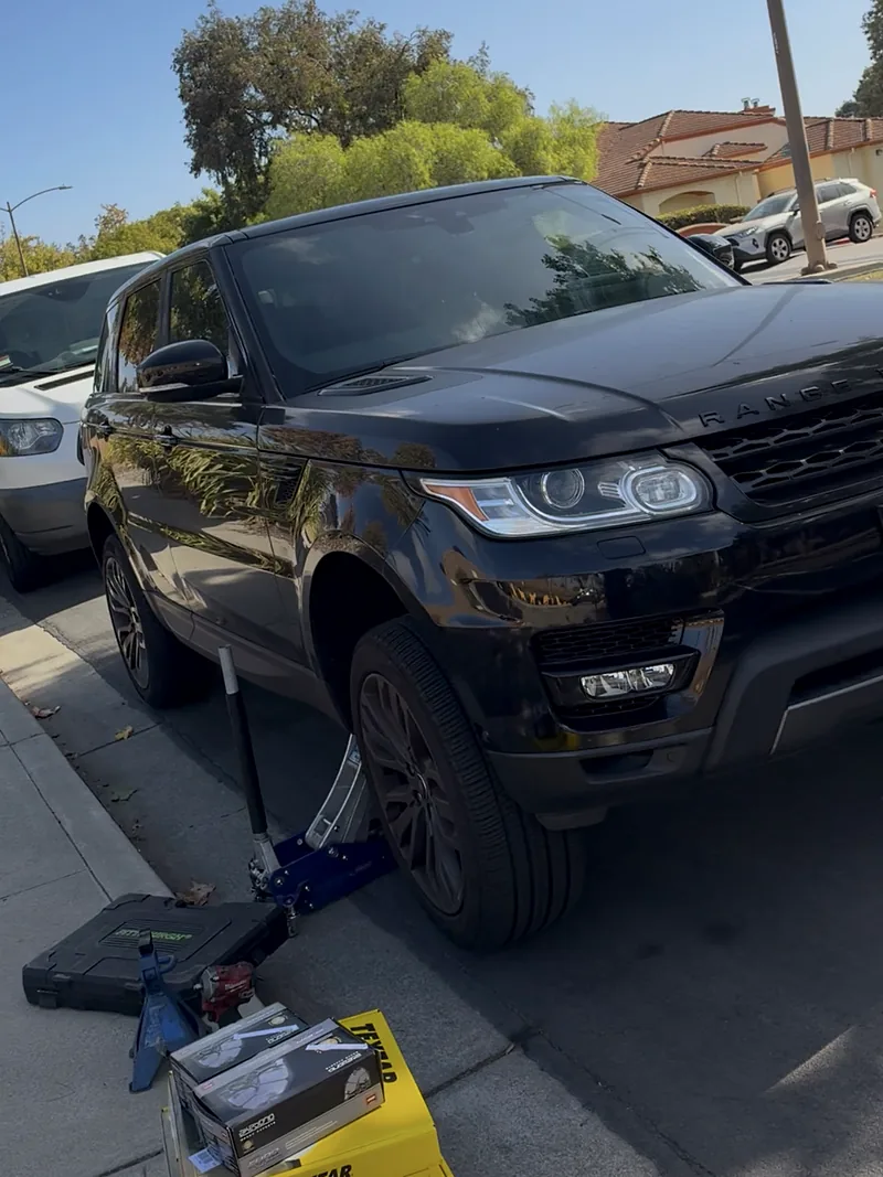 Black Range Rover Sport on a floor jack at the curb with boxes of new parts ready for a mobile repair